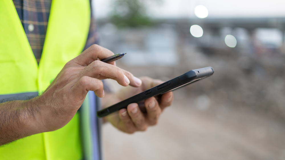 Close up construction worker holding a pen using a smartphone